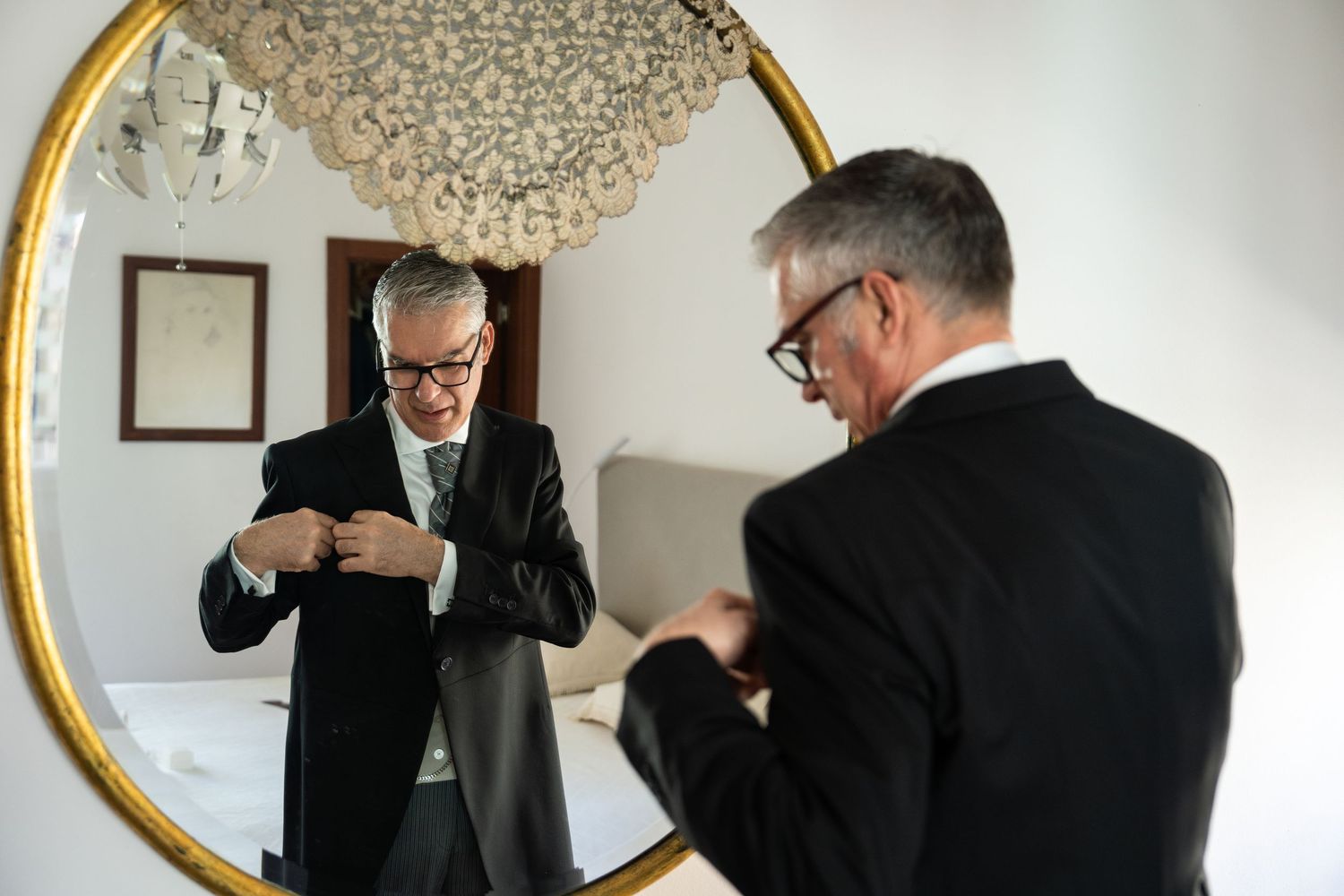Man checking his appearance and adjusting suit in large round mirror.