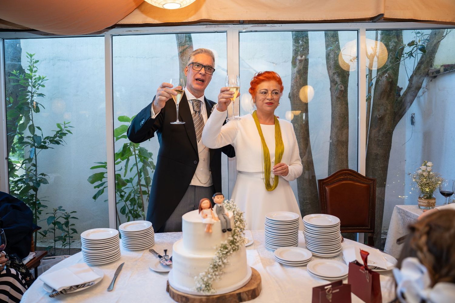 Couple cutting their rustic wedding cake at reception with string lights and outdoor scenery.