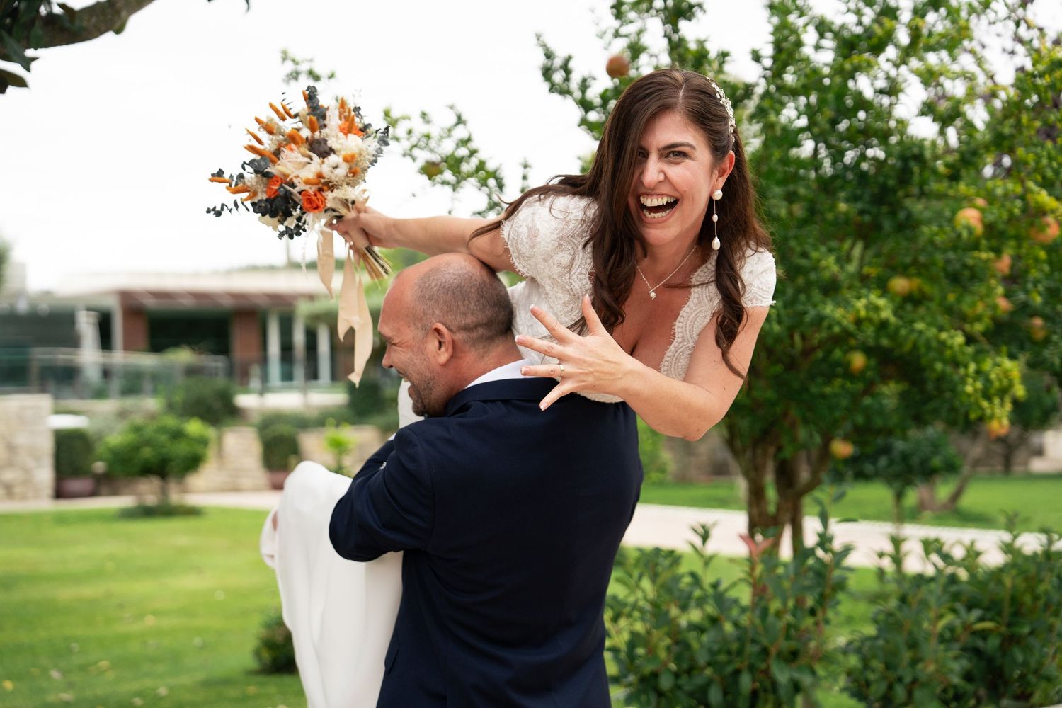A joyful wedding couple dances and celebrates in a sunlit garden setting.