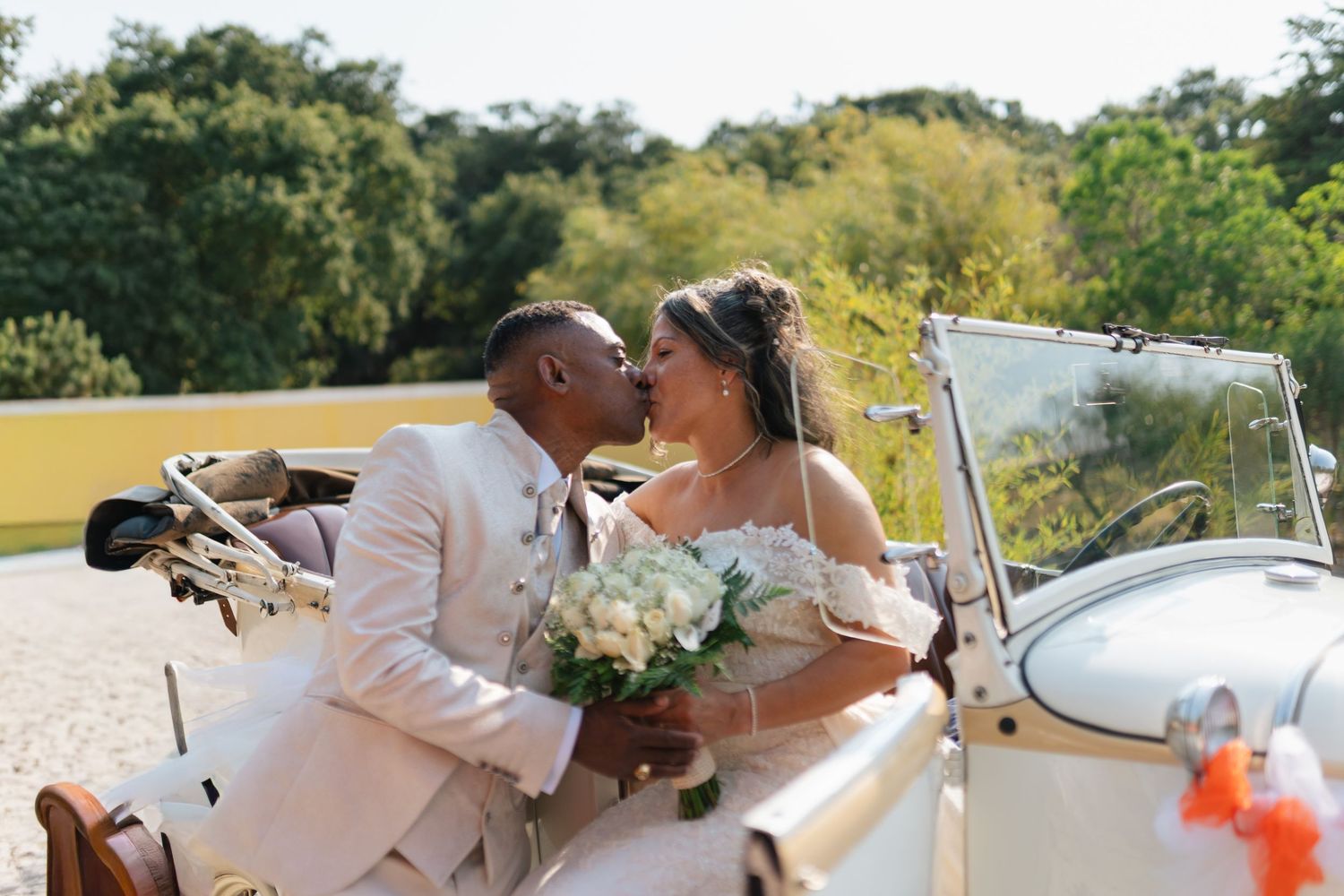 Romantic wedding portraits with vintage white car in outdoor setting.