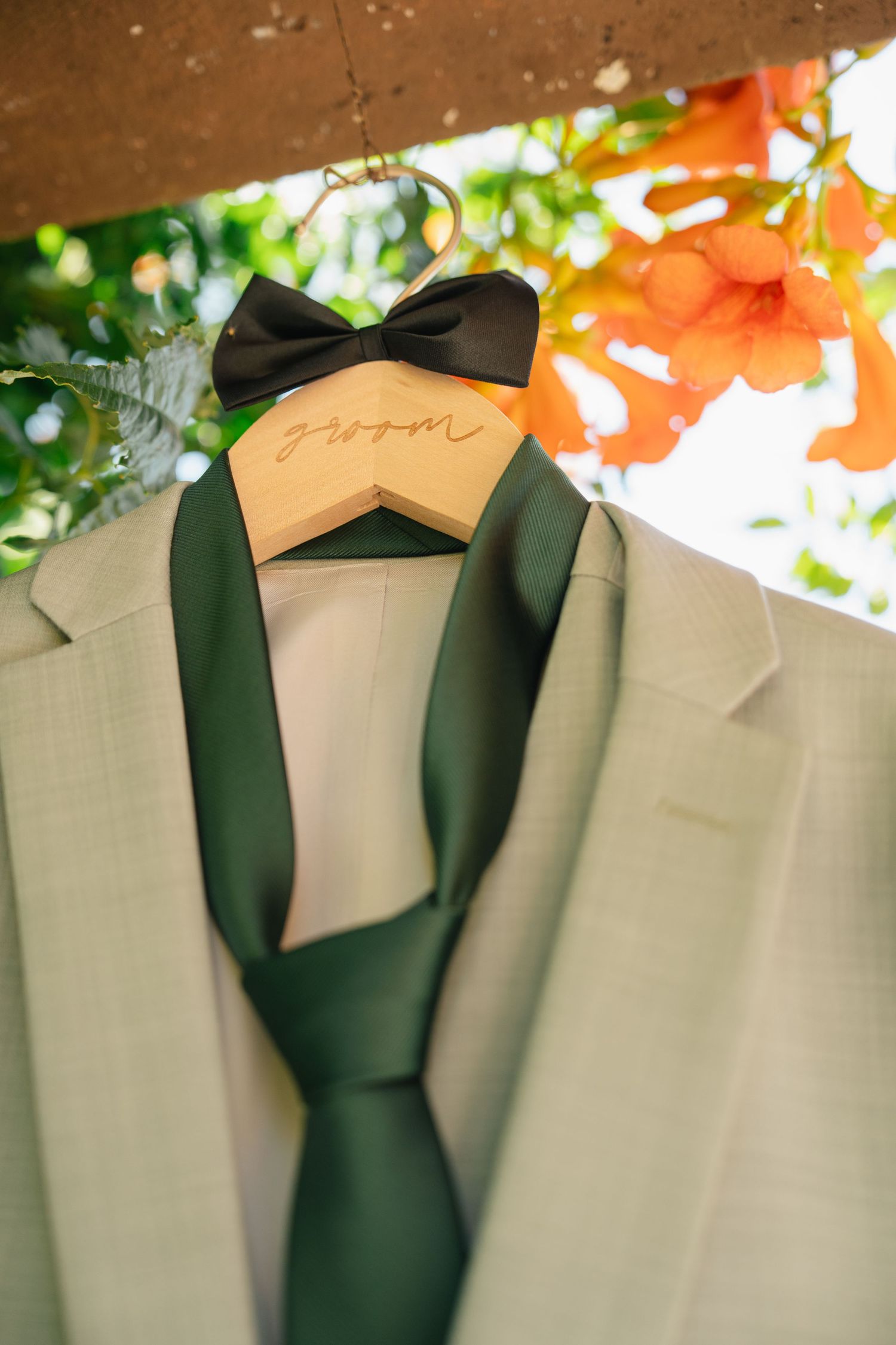 Light sage green suits hanging on wooden hangers against a warm-toned background.
