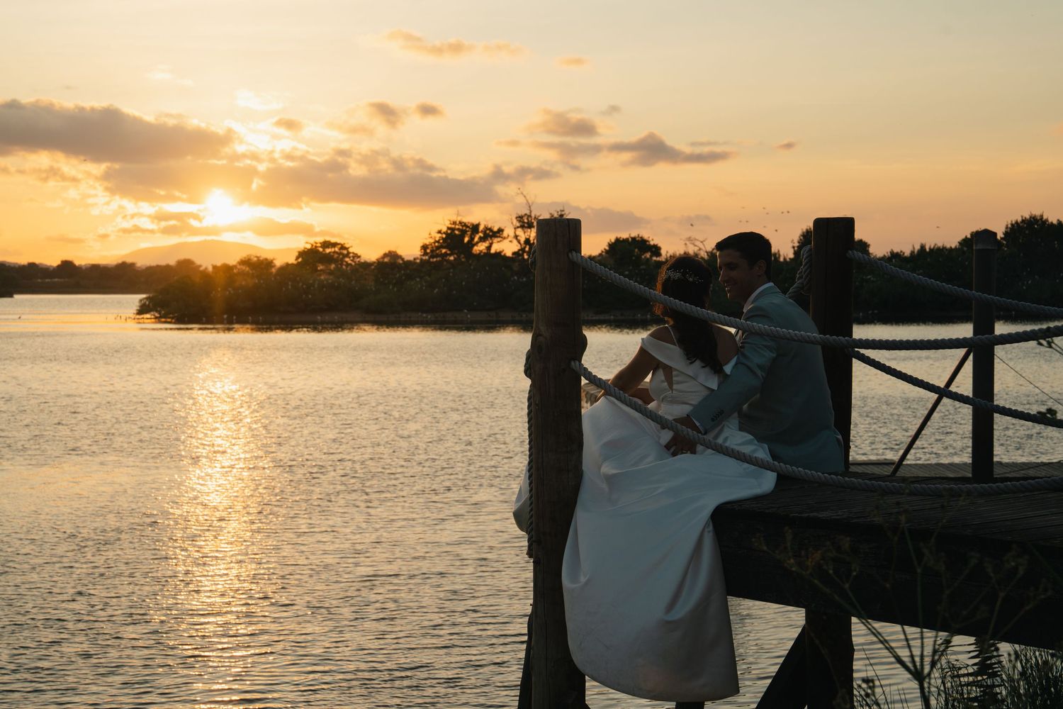 A golden sunset over water creates a romantic backdrop for wedding photos.