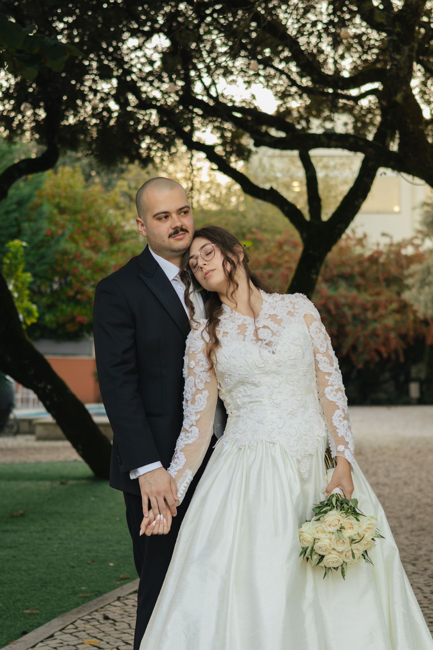 A couple shares an intimate moment under large oak trees during their wedding photoshoot.