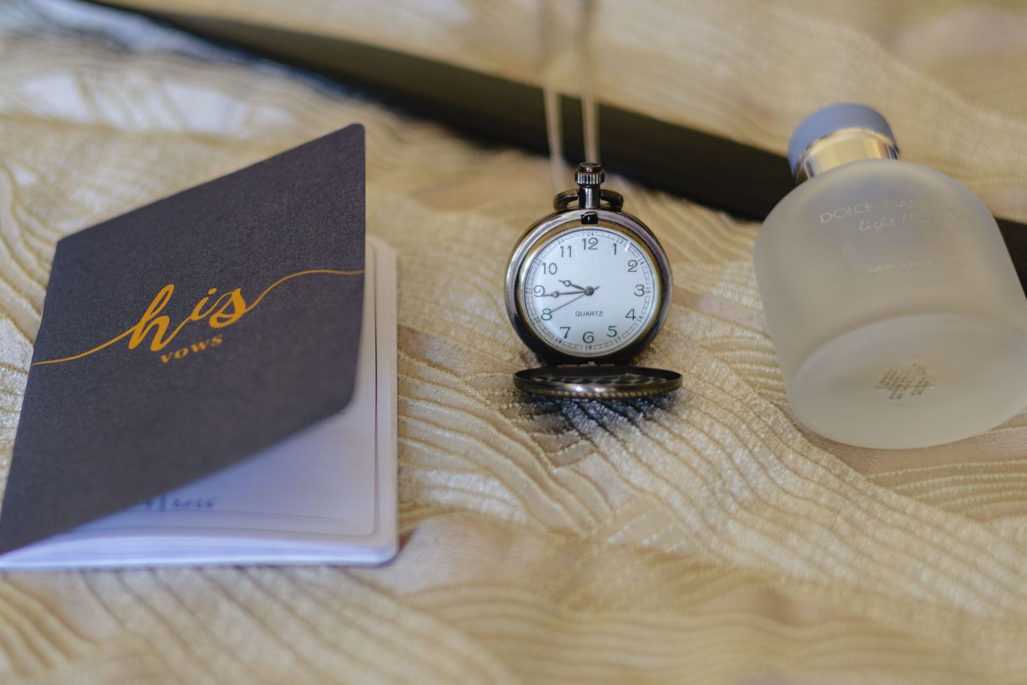 Wedding details including pocket watch and decorative stationery on textured tablecloth.