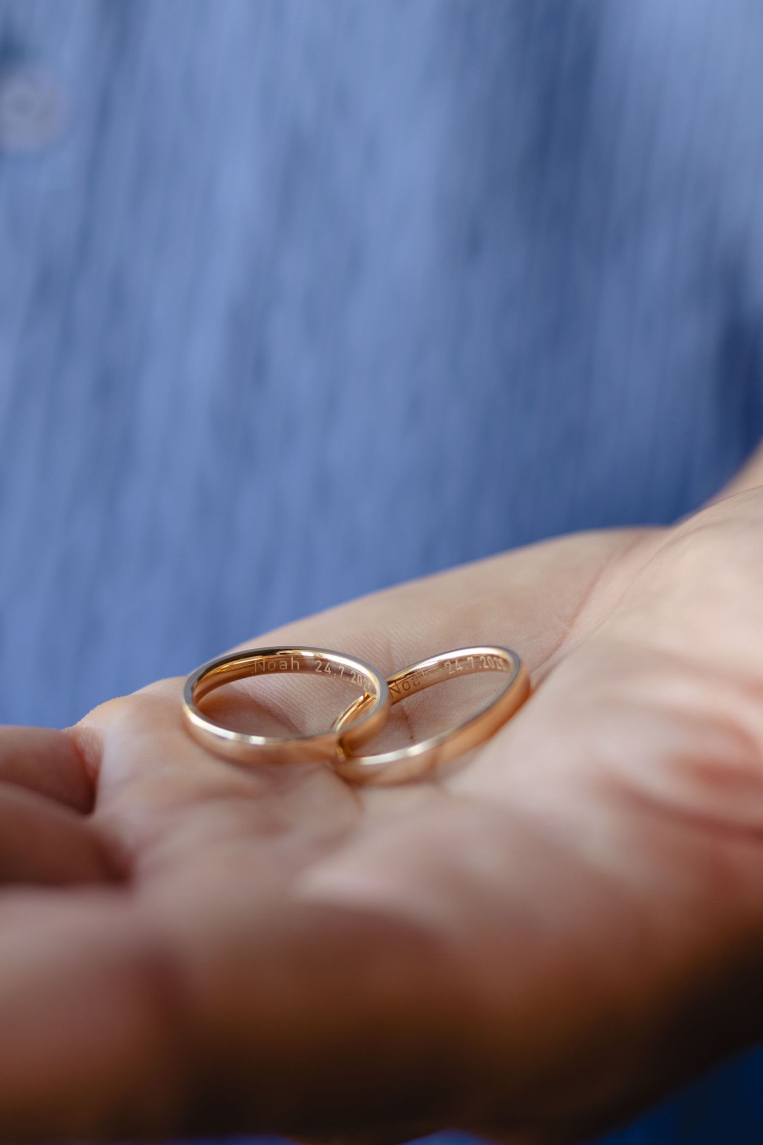 Close-up of delicate gold wedding bands on soft blue background.