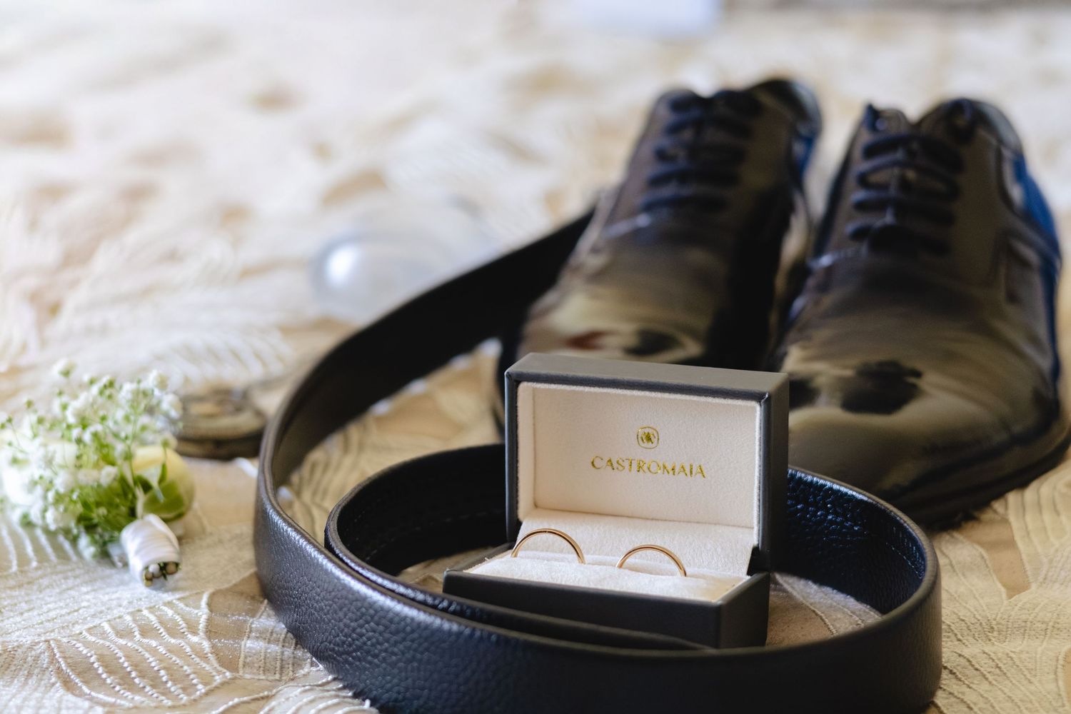 Wedding accessories featuring black dress shoes and ring box on white lace.