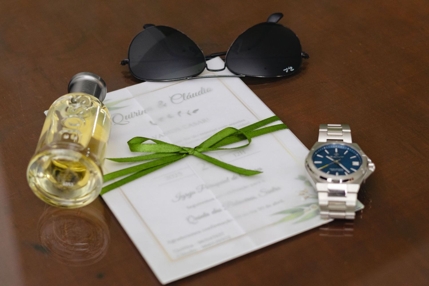 Wedding details including watches, invitations and drinks on a dark wooden surface.