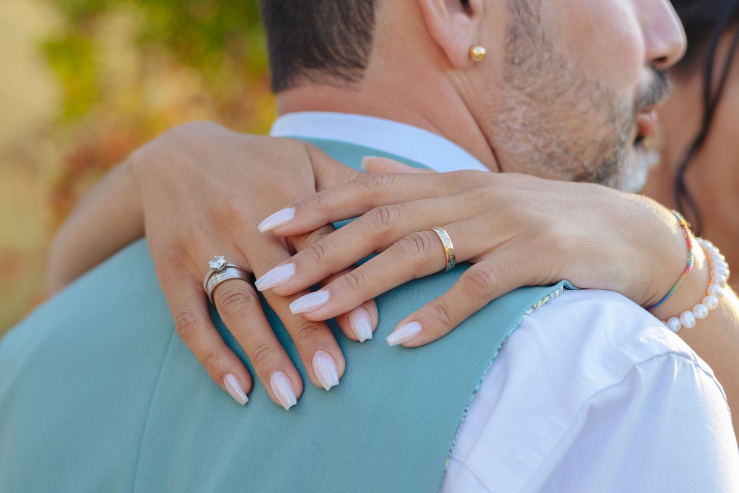 Close up of hands with wedding rings embracing against a turquoise suit jacket.