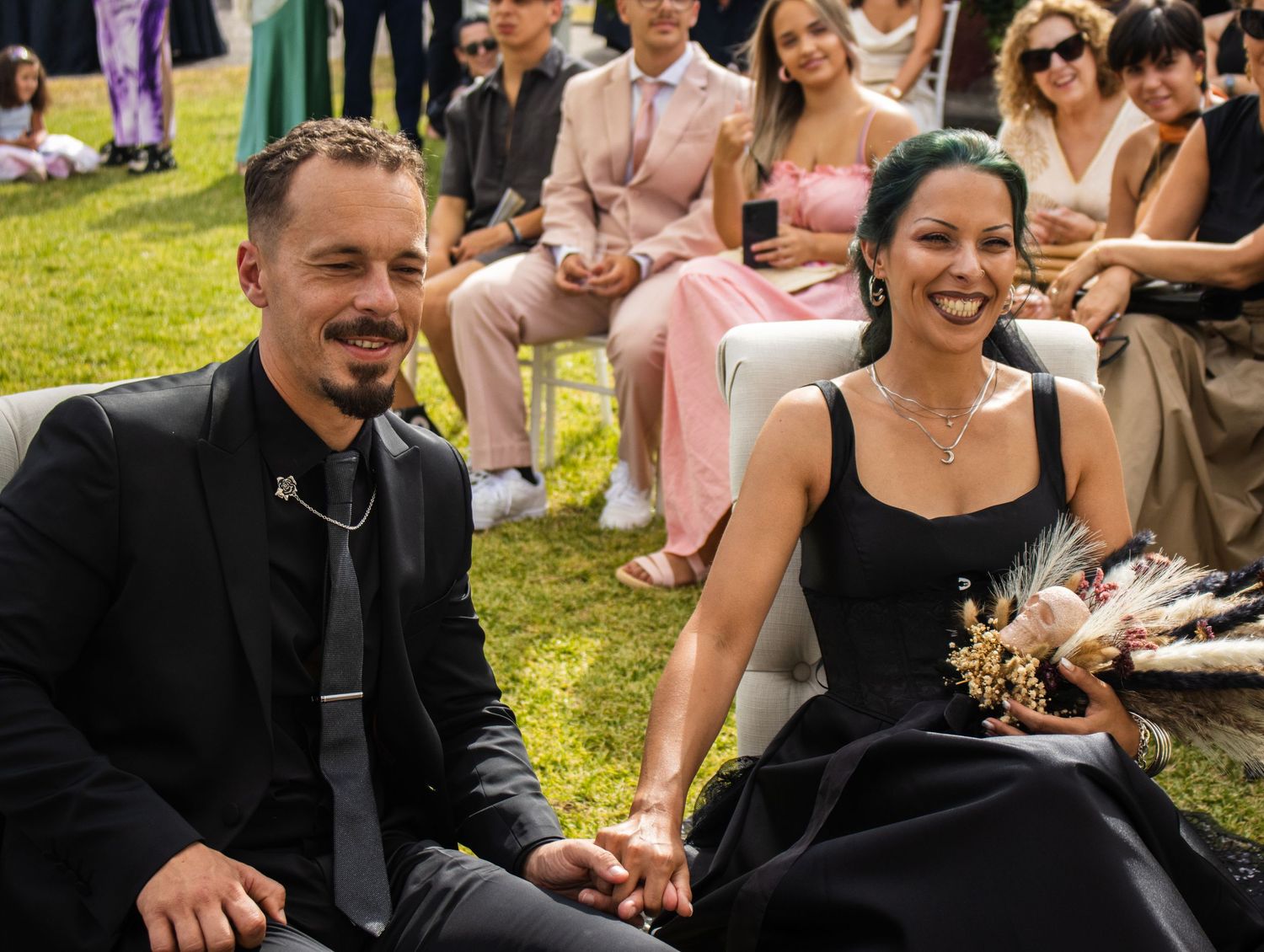 Wedding guests in formal attire sitting on lawn chairs during outdoor ceremony.