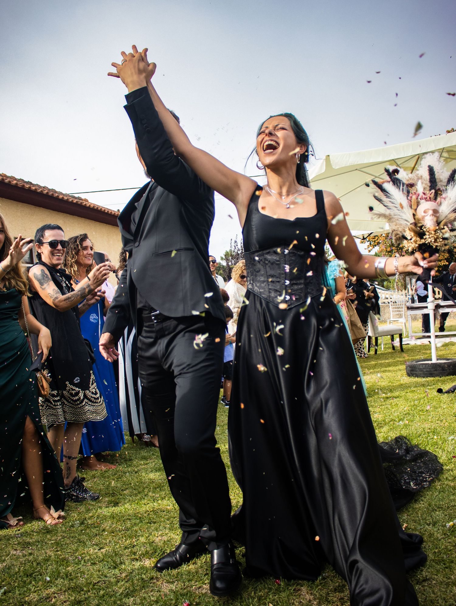 Joyful couple celebrating with raised hands as confetti falls at outdoor wedding.
