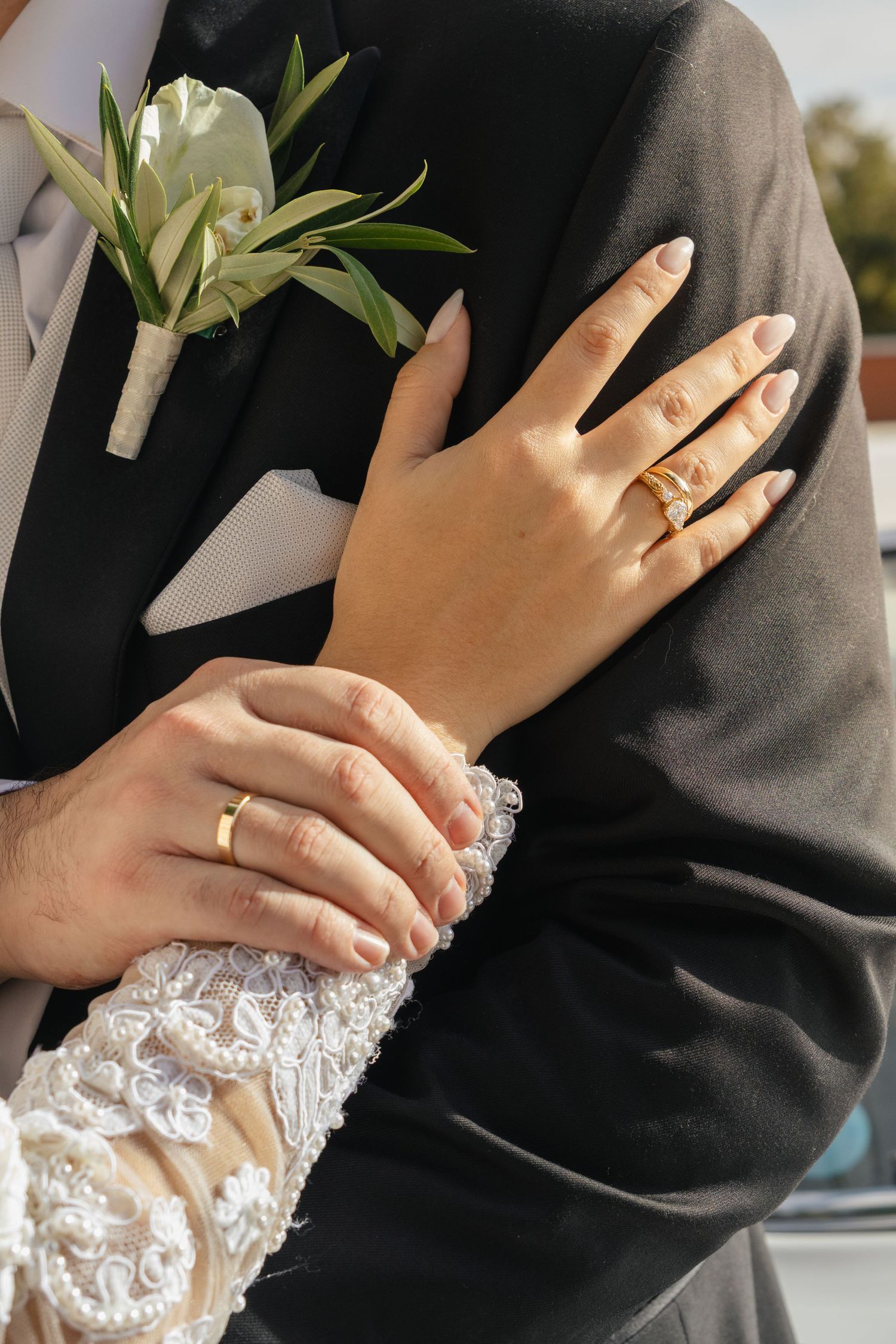 Close-up of hands wearing wedding rings against black fabric and white lace details.