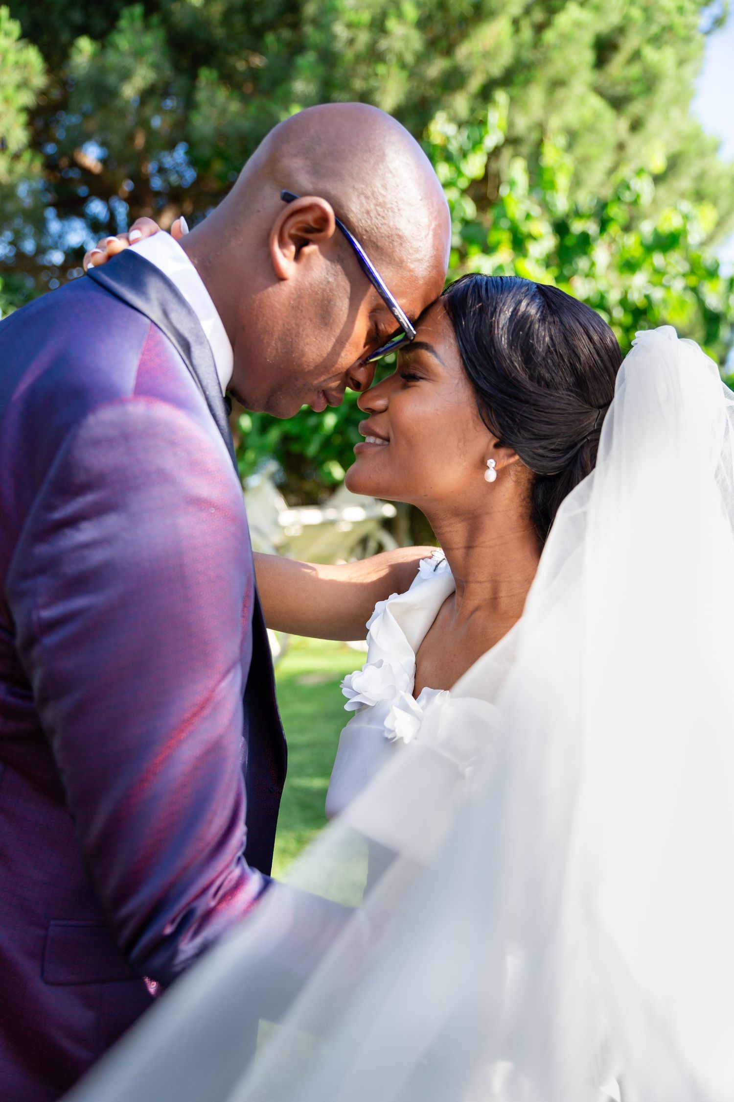 A newlywed couple shares a romantic moment outdoors surrounded by lush greenery.