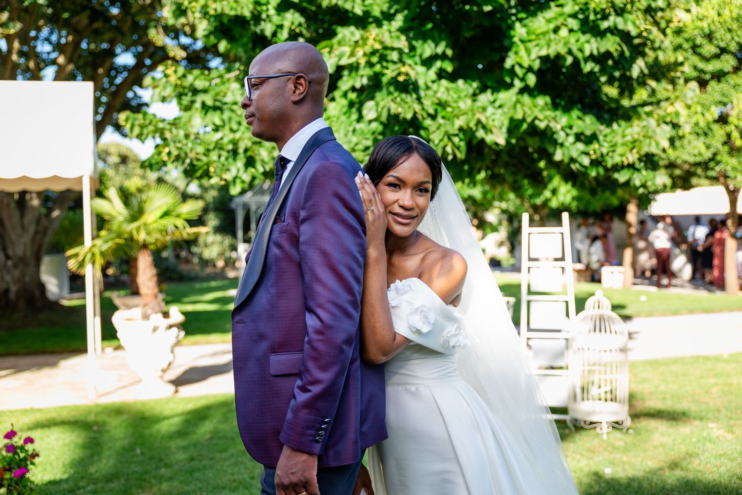 Wedding couple embraces and laughs together in a sunny garden setting.