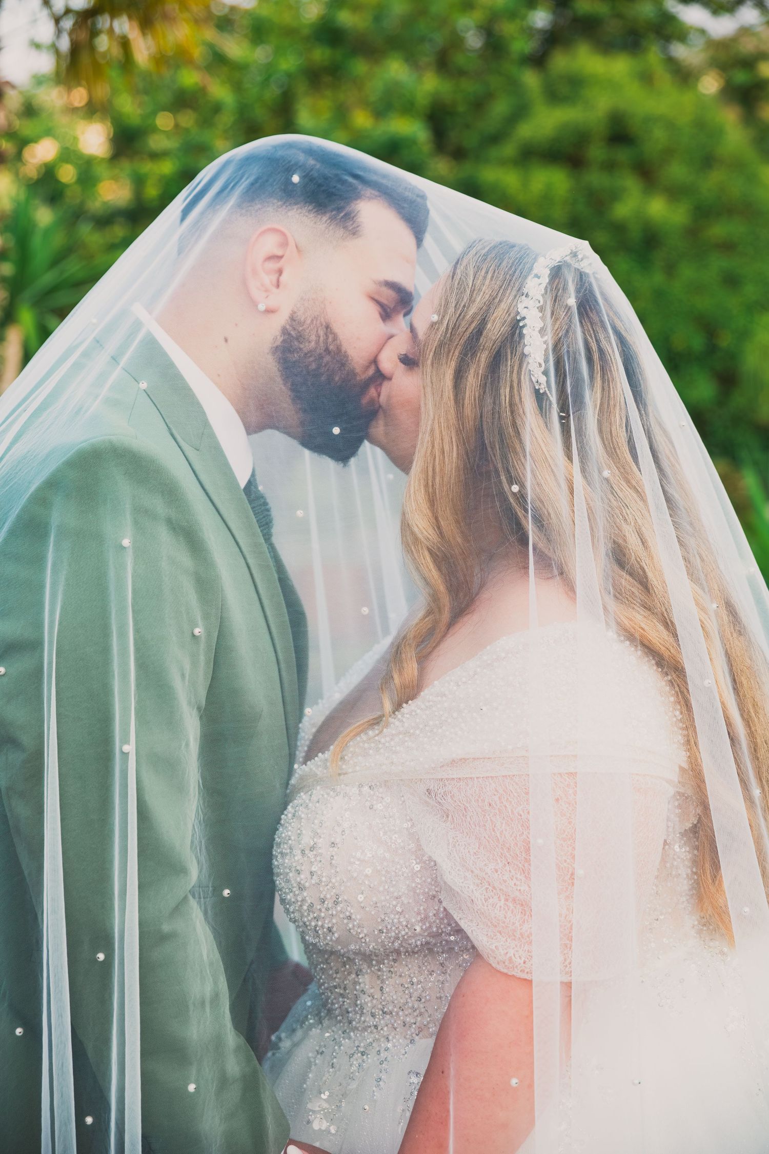 Romantic wedding portraits through sheer veil in garden setting.