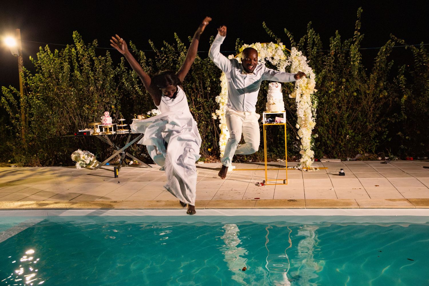 Wedding couple dances near sparkling fountains and a pool during their evening celebration.