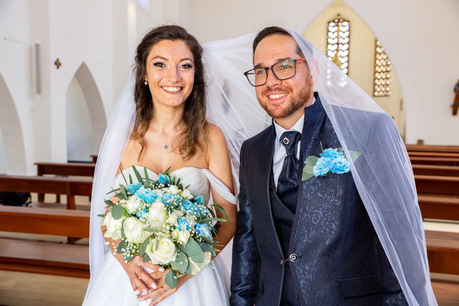 Wedding portraits taken inside a bright church with decorative windows and floral arrangements.