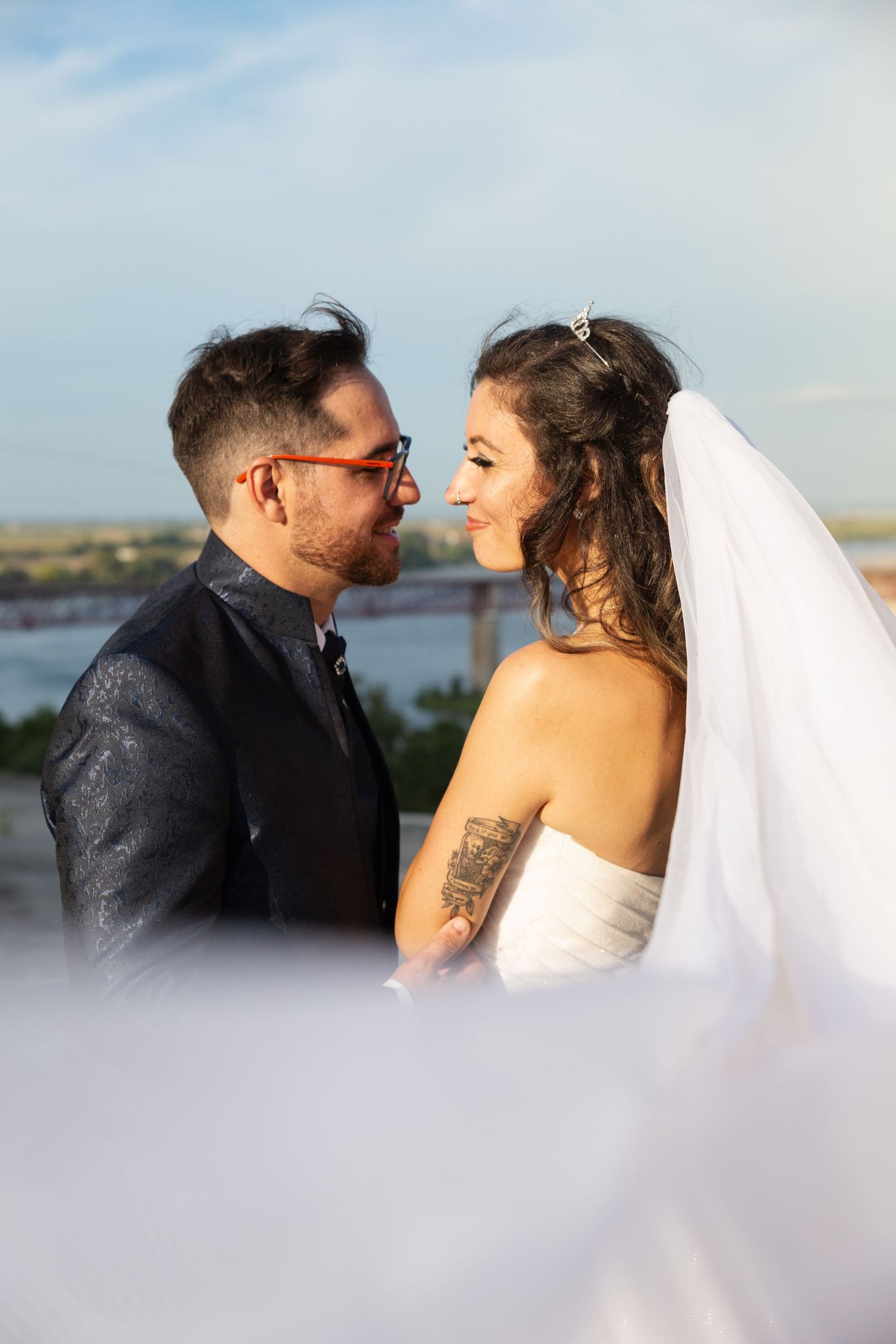 Wedding couple shares intimate moments against a waterfront backdrop with flowing veil details.
