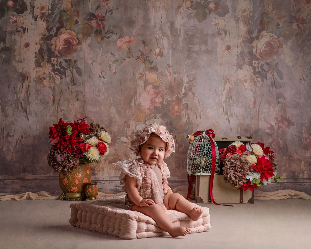 Vintage styled nursery scene with floral backdrop, decorative lantern and red rose arrangements on textured floor.
