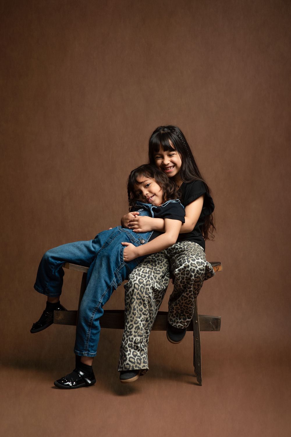 A series of artistic studio portraits showing tender moments between two people sitting on a wooden bench against brown backdrop.