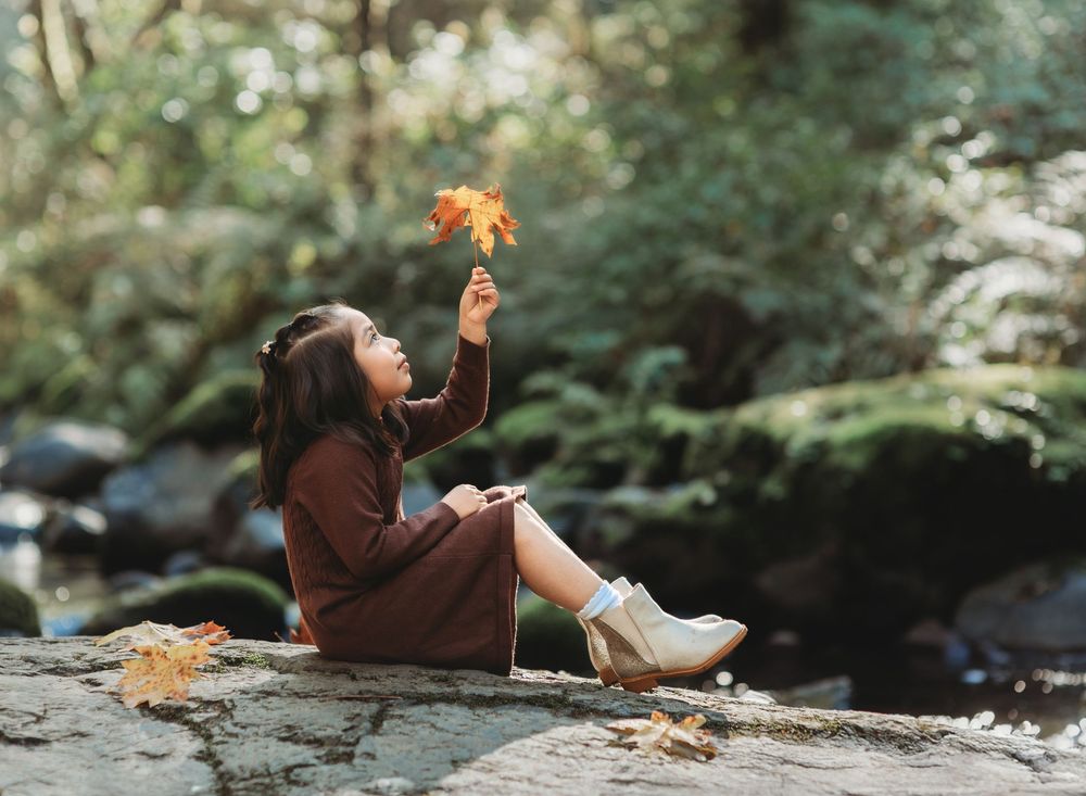 A person in brown clothing lies on the ground while playing with autumn leaves in a tranquil forest setting.