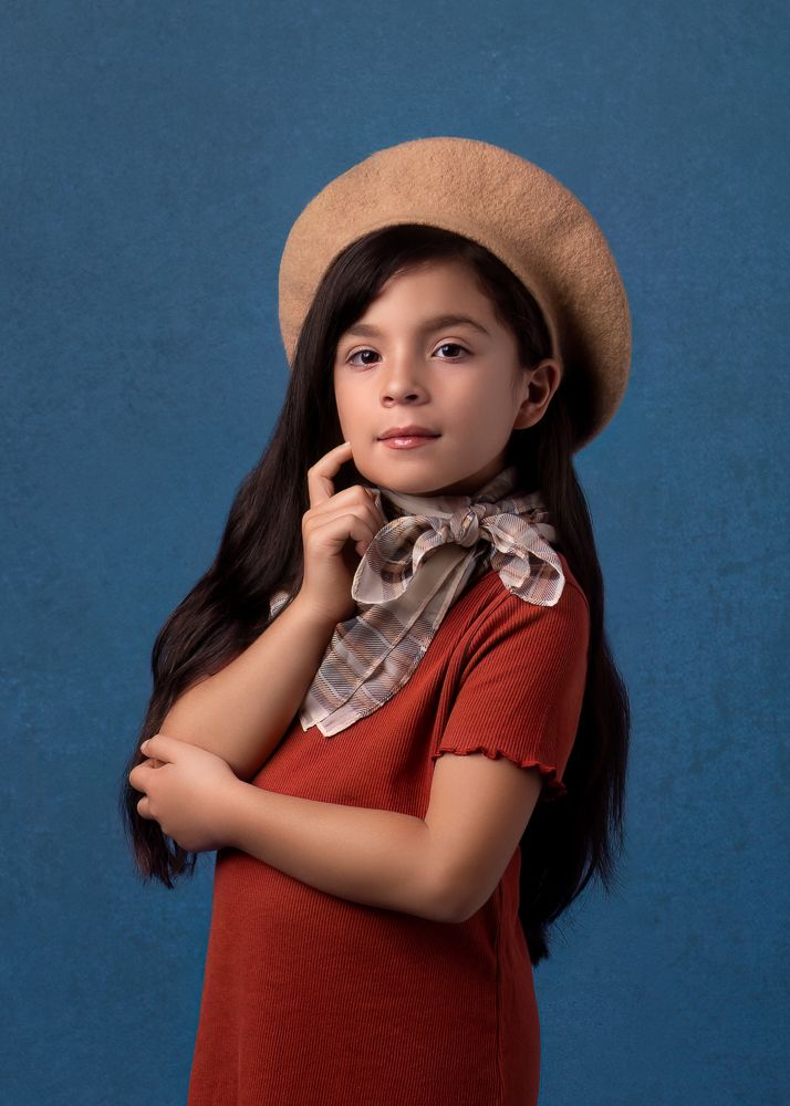 Portrait wearing beige beret and red top against blue backdrop.
