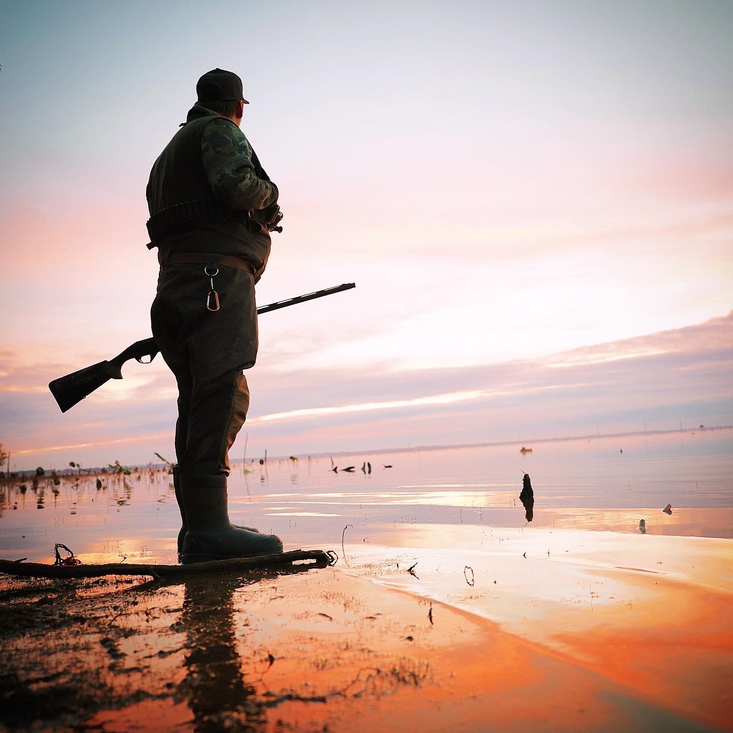 Silhouettes of hunters standing in shallow water during vibrant sunset.