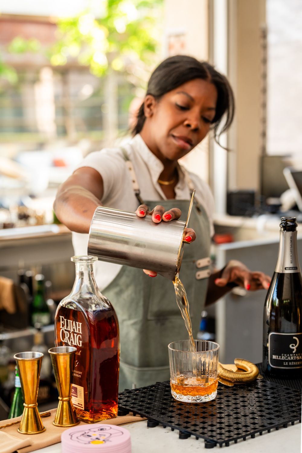 Bartender pouring a cocktail with measuring tools and bottles on counter.