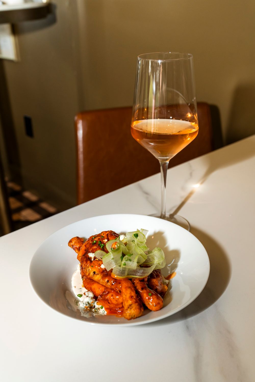 Buffalo wings with celery sticks and blue cheese dressing served with a glass of rose wine on a white plate.