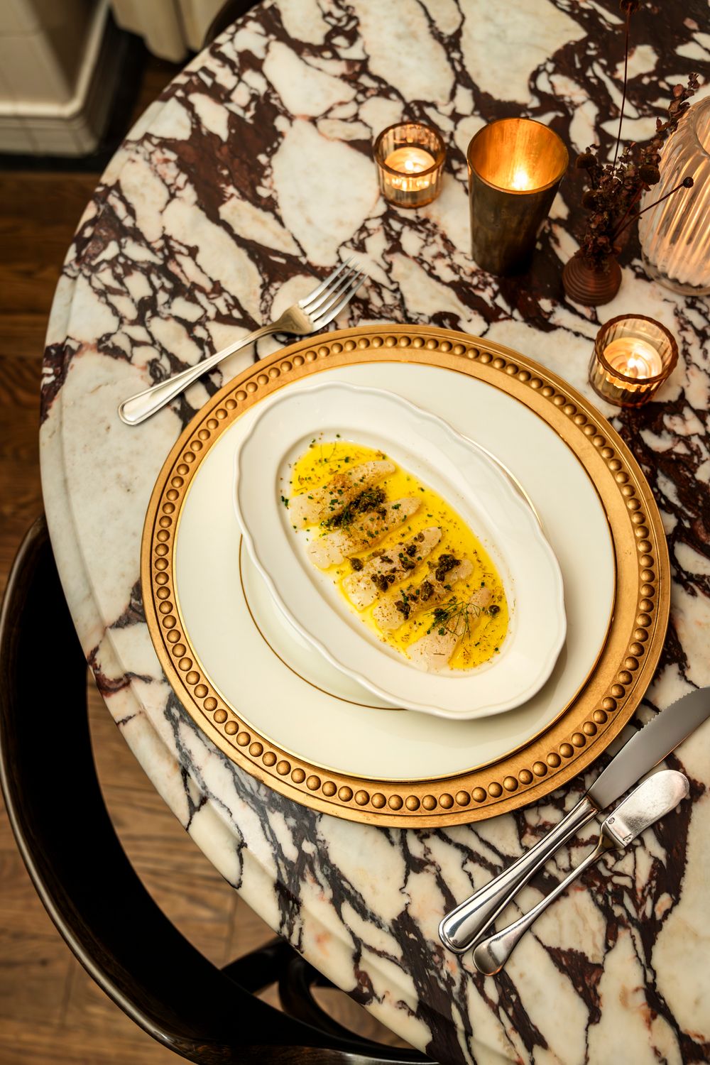Elegant table setting with yellow pasta dish on gold-rimmed plates atop marble surface with glowing candles.