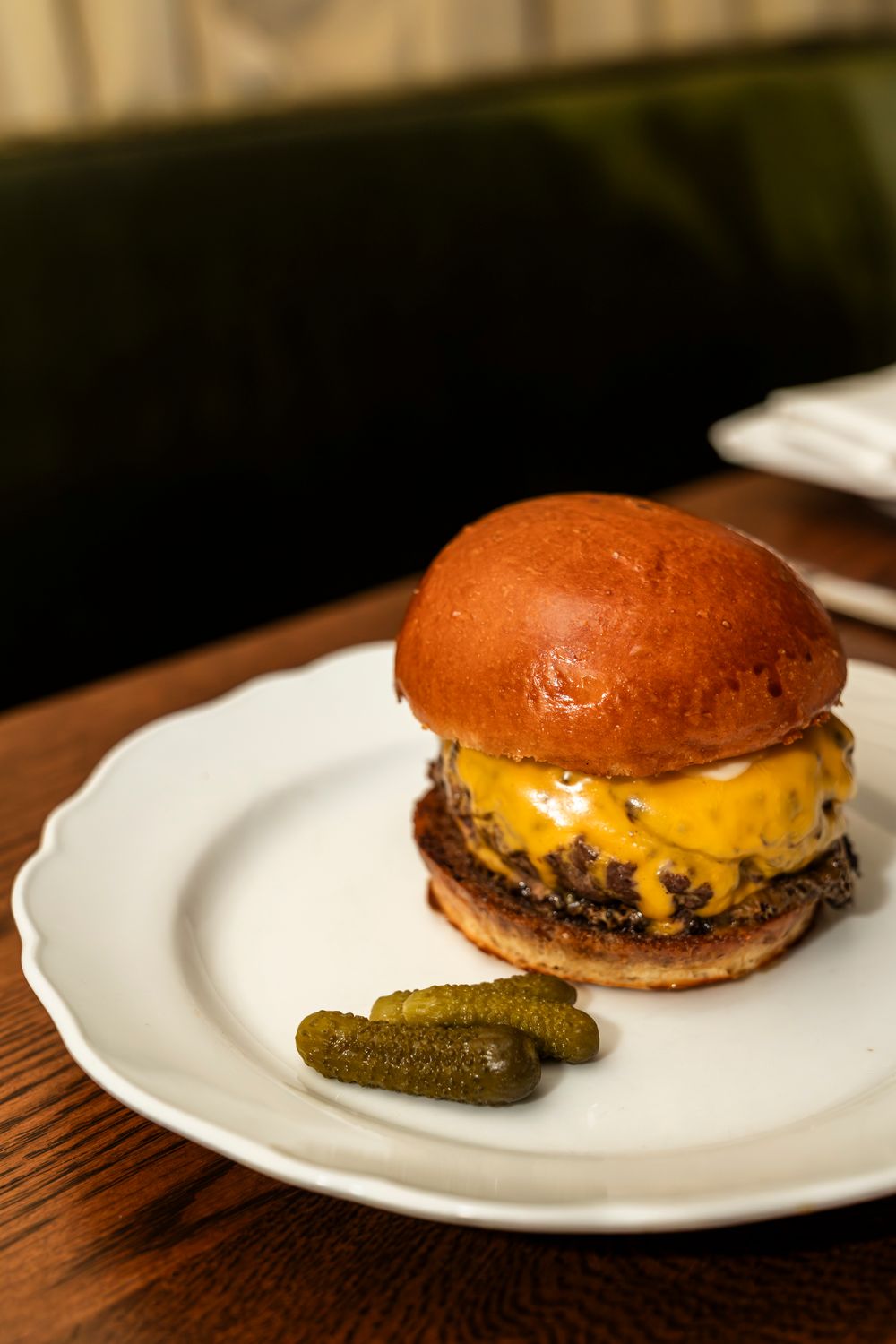 Juicy cheeseburger with melted cheese and a pickle served on a white plate with a wooden table background.