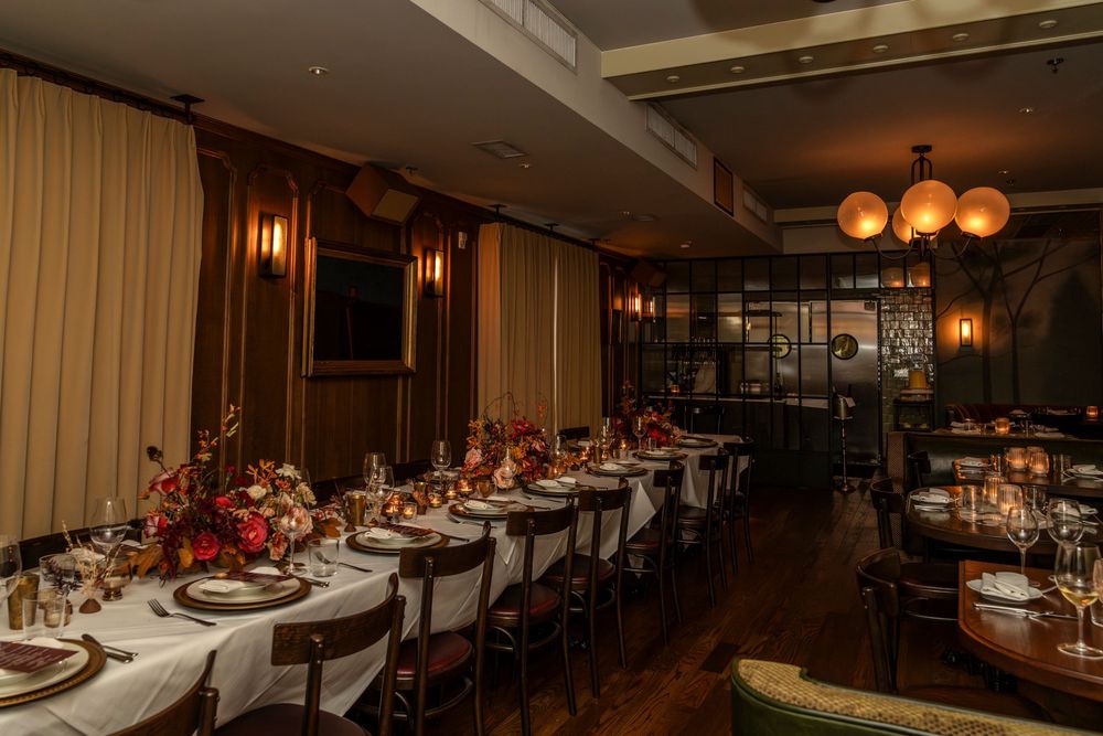 Elegant restaurant interior with warm lighting, dark wood tables, and red accents creating an intimate dining atmosphere.