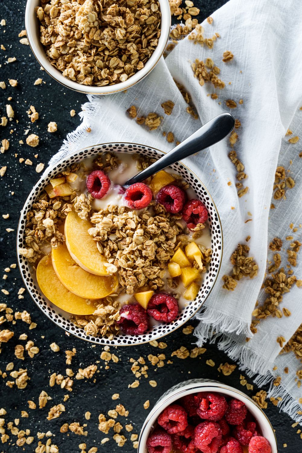 Healthy breakfast bowl with granola, fresh raspberries, and sliced peaches on dark background.