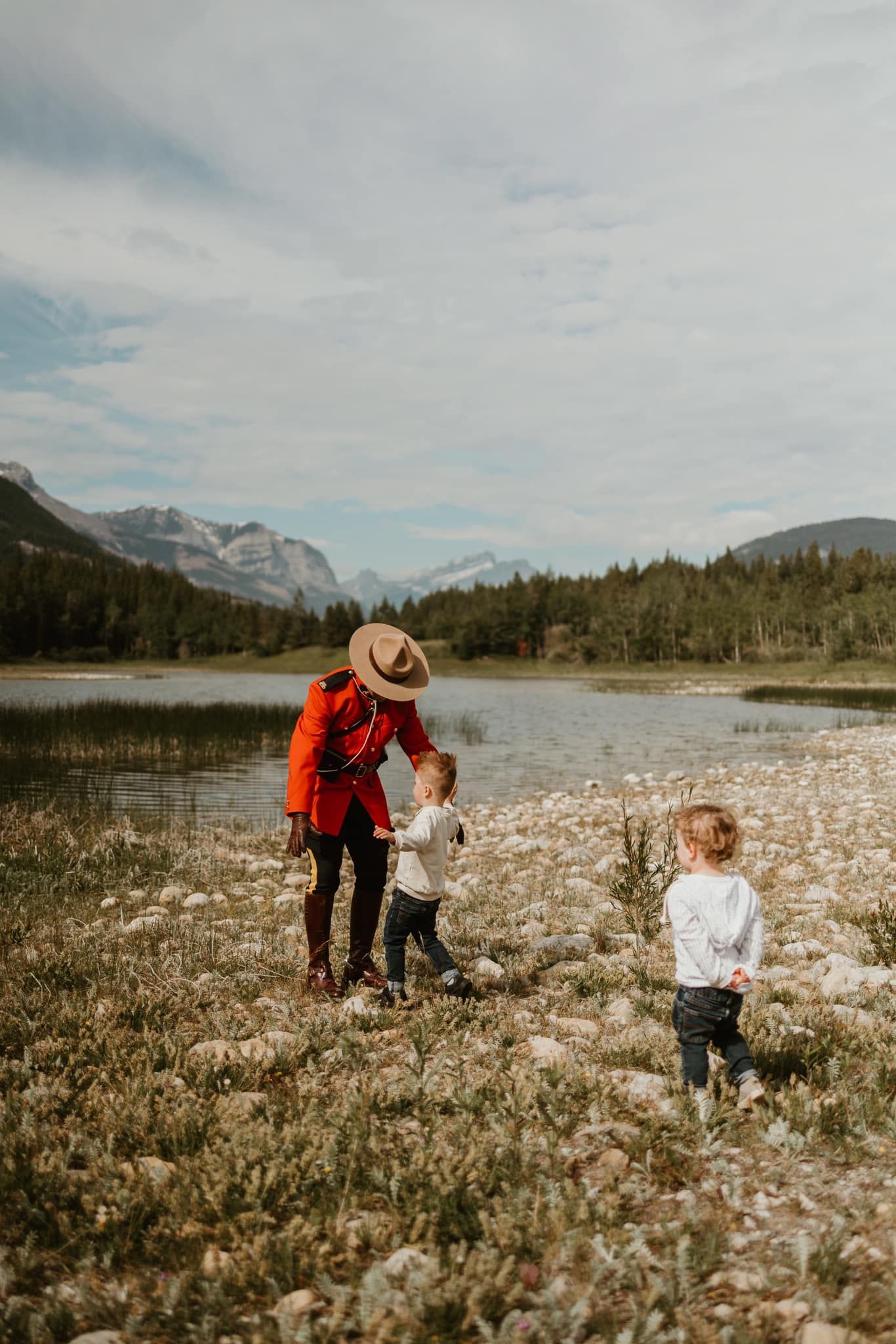 Family exploring wildflower meadow with mountain lake backdrop.