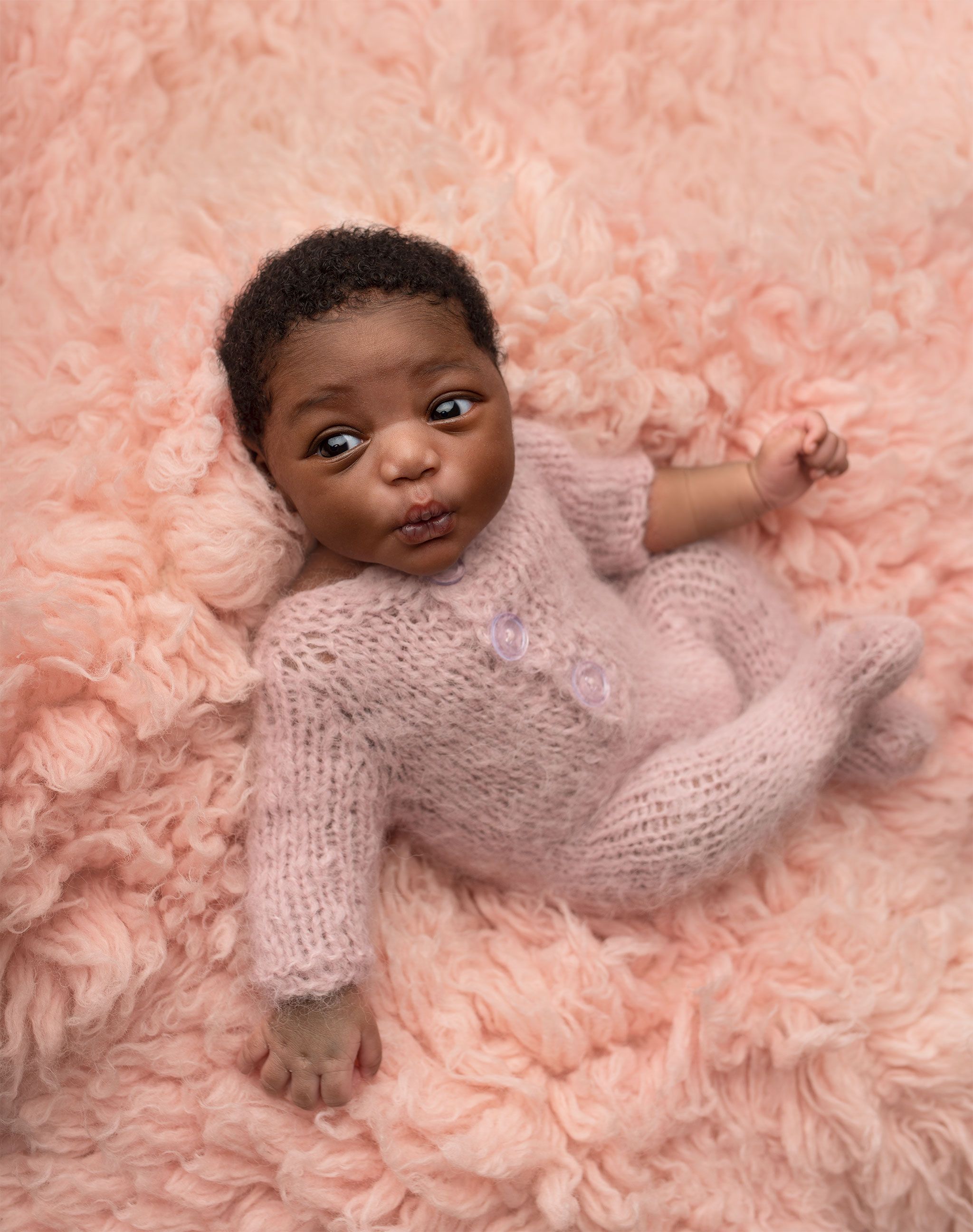 Sweet sleeping newborn baby resting on a soft pink blanket wearing a knitted pink onesie.