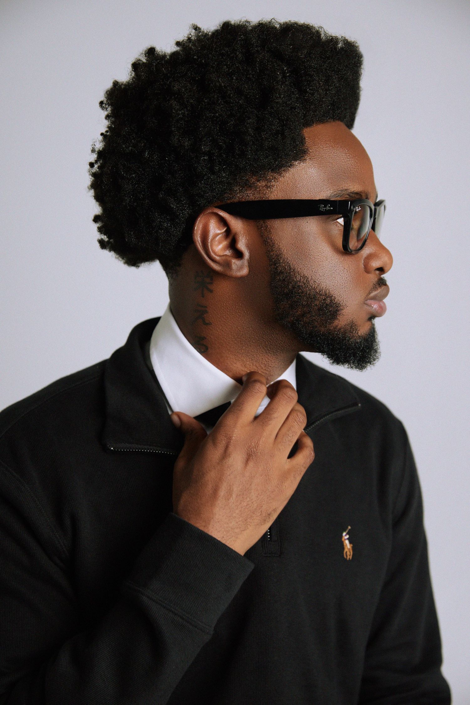 Profile view of person with curly afro hair wearing glasses and black turtleneck against white background.