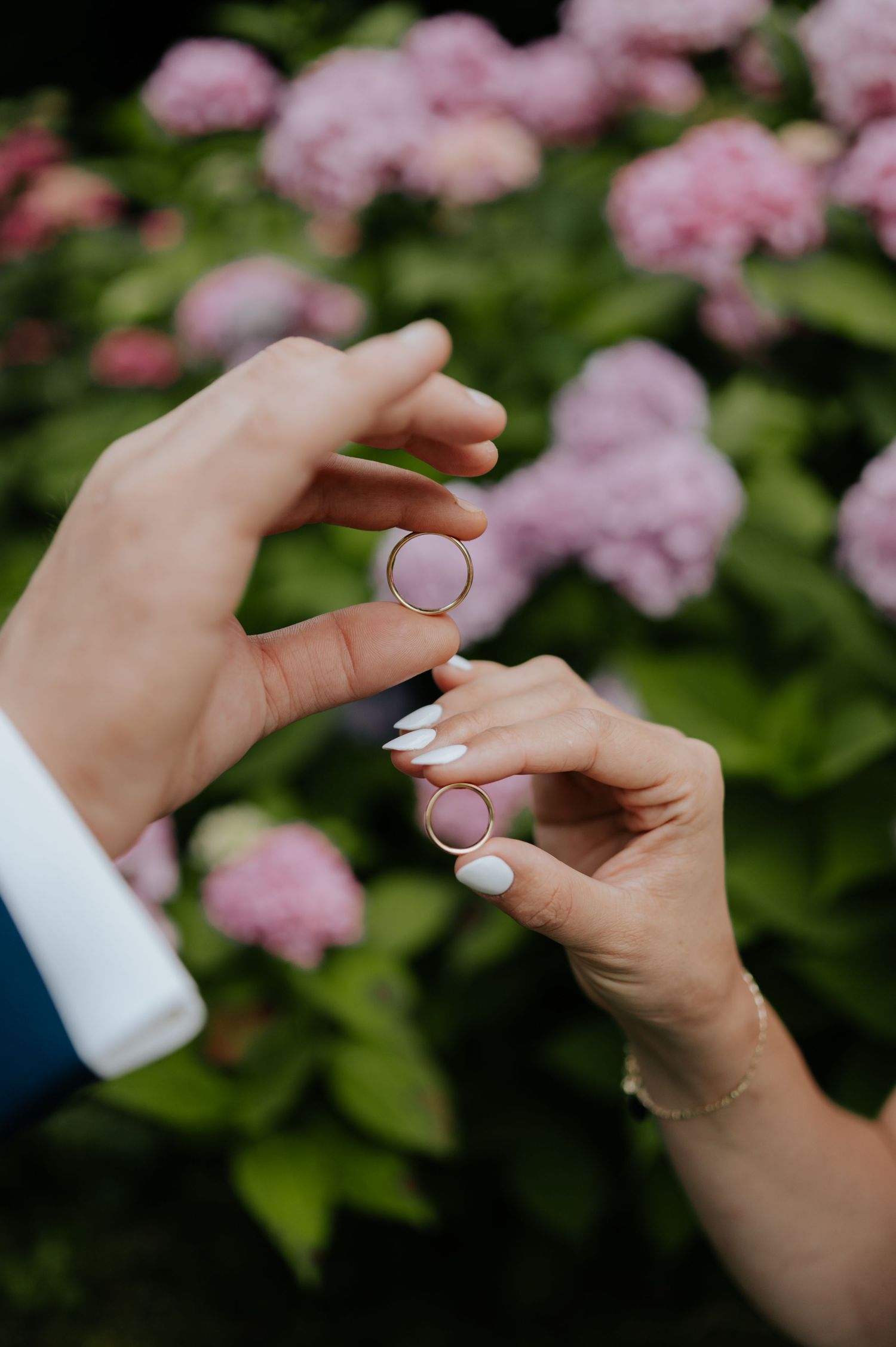 Hände, die Ringe halten vor einem verschwommenen rosa Blumengartenhintergrund.