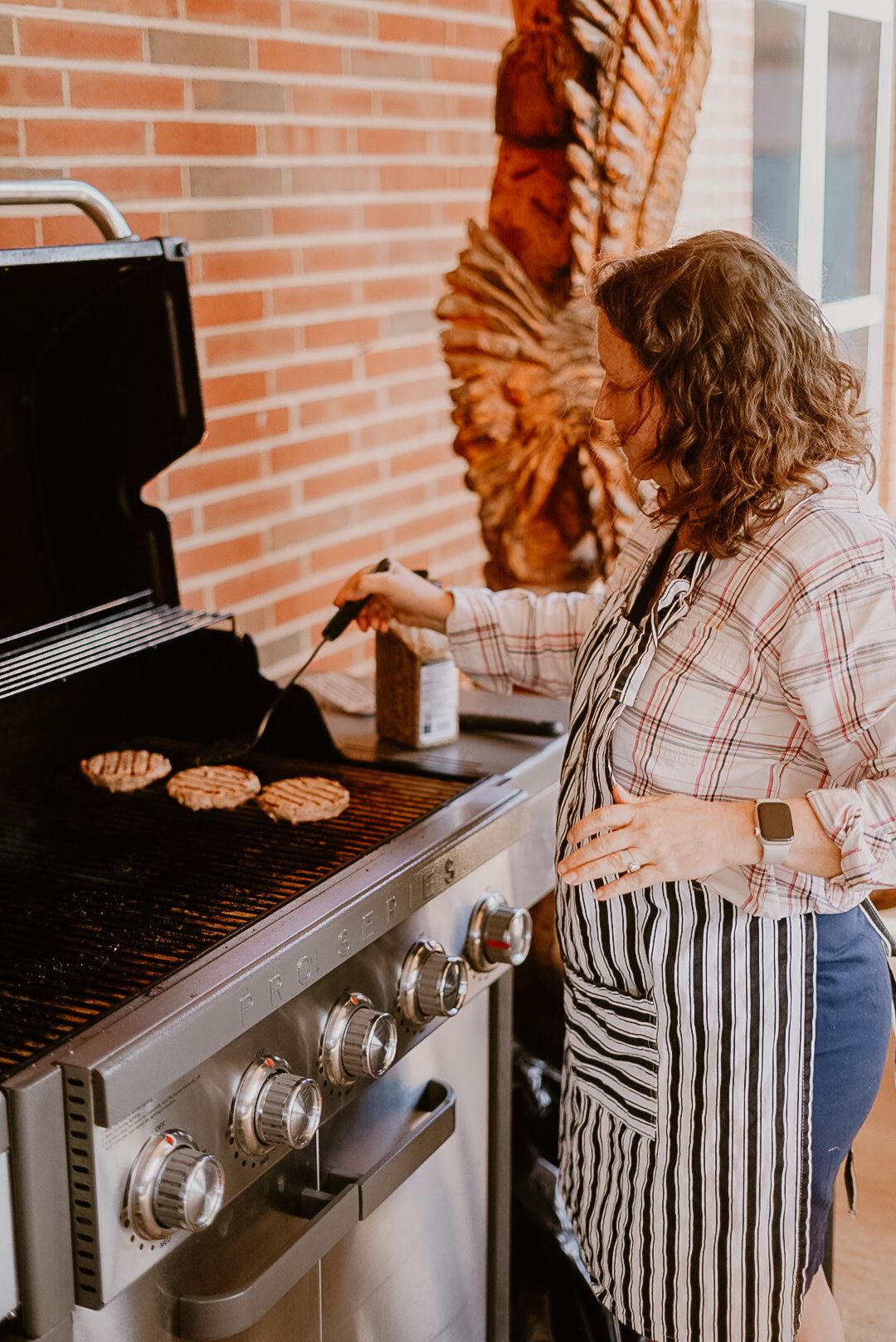 Person in striped apron grilling burgers on outdoor gas grill.