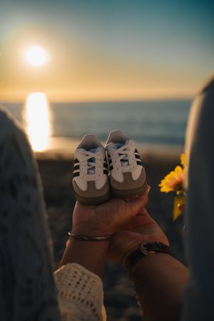 Baby shoes silhouetted against a sunset ocean horizon create a tender moment at the beach.