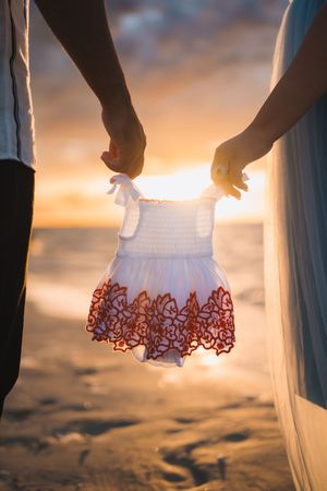 A person in a white dress holds up the lace hem of their gown against a golden sunset beach backdrop.