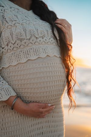 Close-up series of a pregnant woman's belly in a white crochet dress against a sunset sky background.