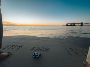 Wide angle panoramic view of a sandy beach at sunset with calm ocean waters and clear blue sky.