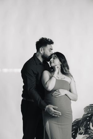 A romantic black and white maternity photoshoot features a couple embracing in tender moments against a light background.