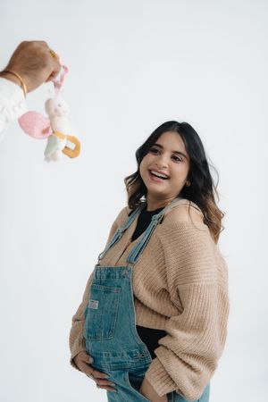 Playful lifestyle photos of someone in denim overalls and tan sweater making expressions while holding an orange.