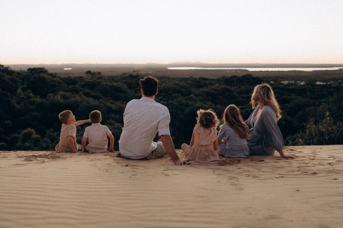 Group sits together on sandy dune overlooking scenic landscape at sunset.
