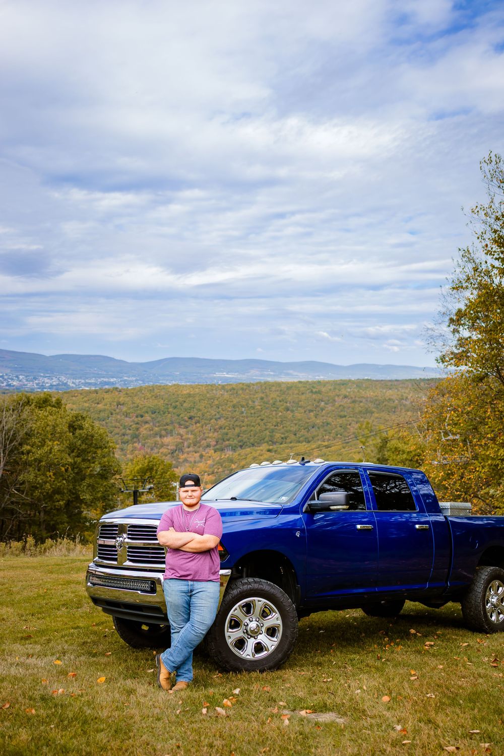 Senior boy poses with his truck at a hill looking over the city