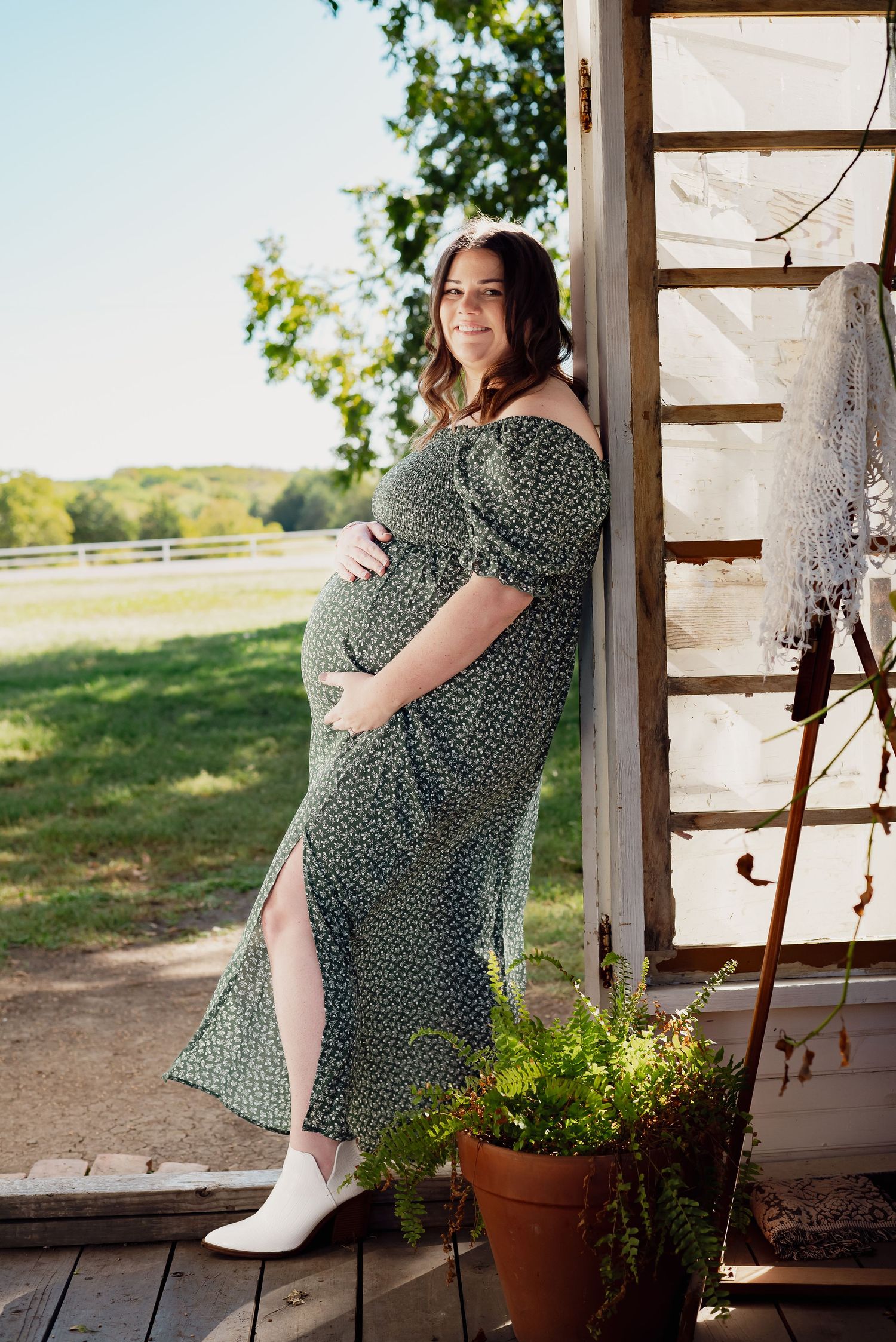 A woman in a polka dot dress sits on a rustic porch with potted plants.