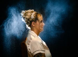 Dramatic side profile portrait with blue powder effect in dark studio setting.