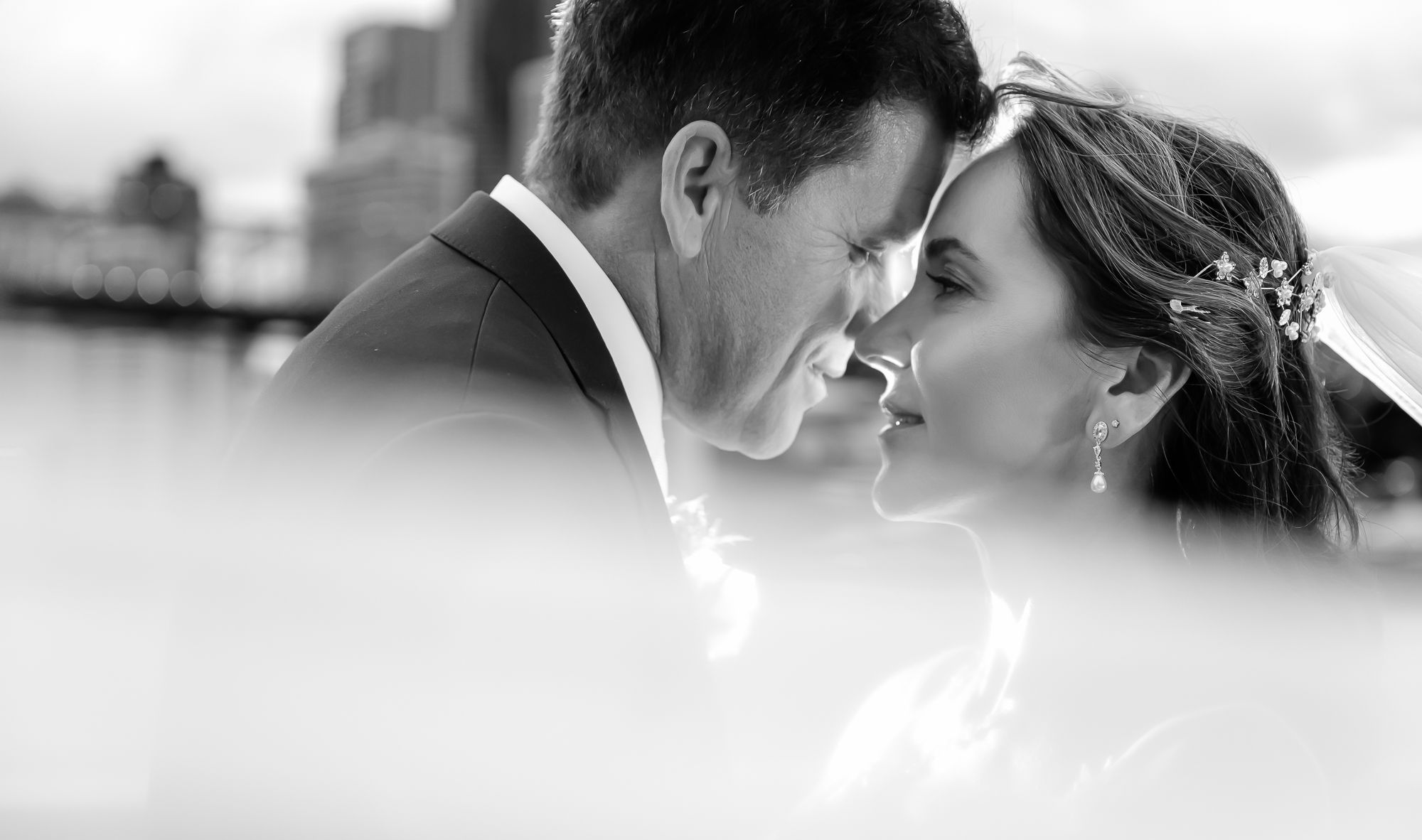 A romantic black and white wedding photograph showing a tender intimate moment between newlyweds.
