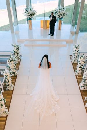 Aerial view of a wedding ceremony in a modern chapel with white floors, glass walls and floral arrangements.