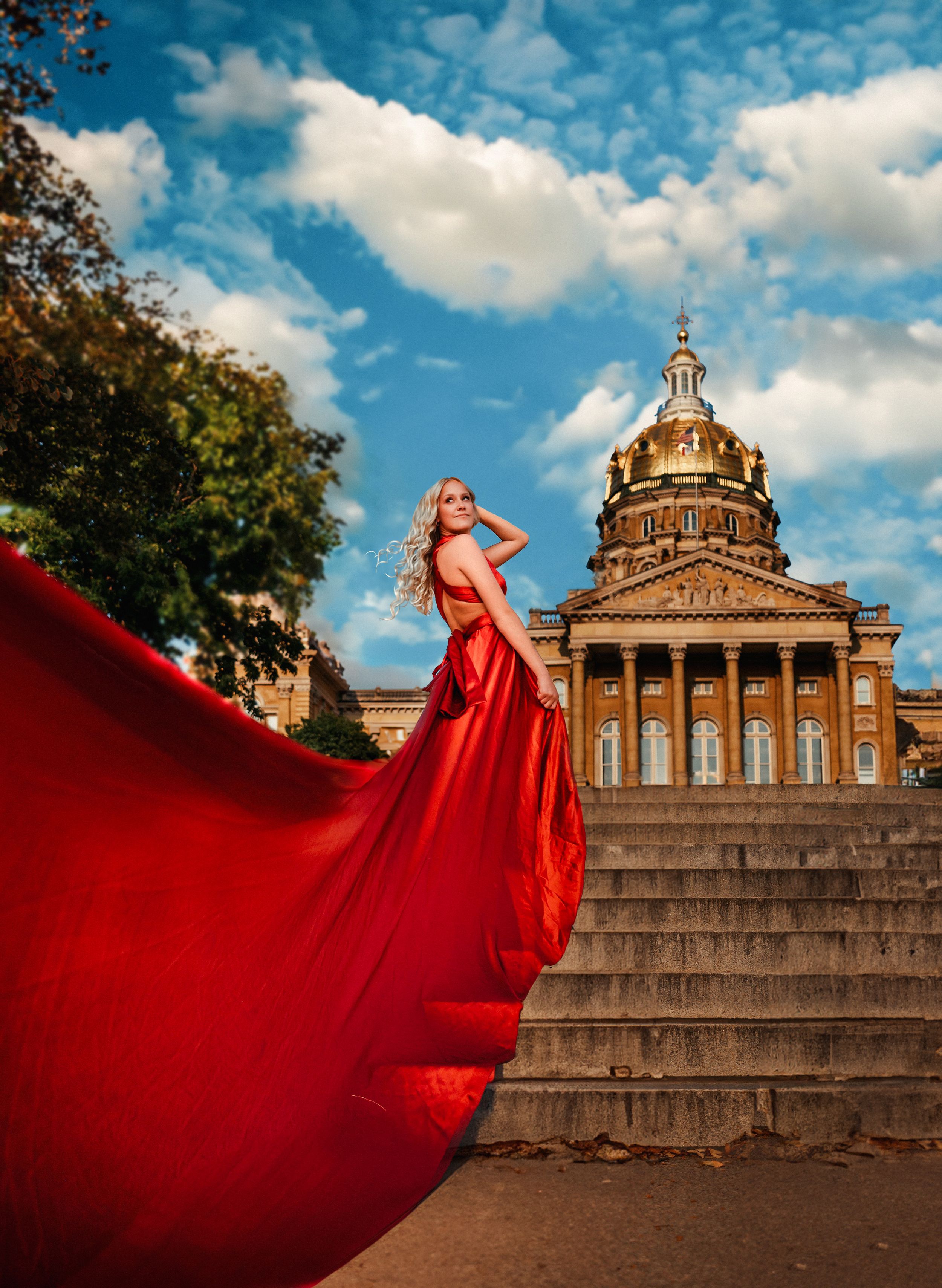 Woman in flowing red gown standing on steps before grand capitol building dome.